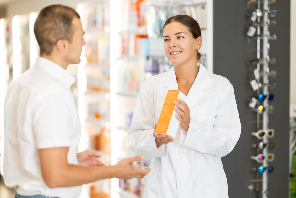 Female pharmacist consulting young guy about medicament in box