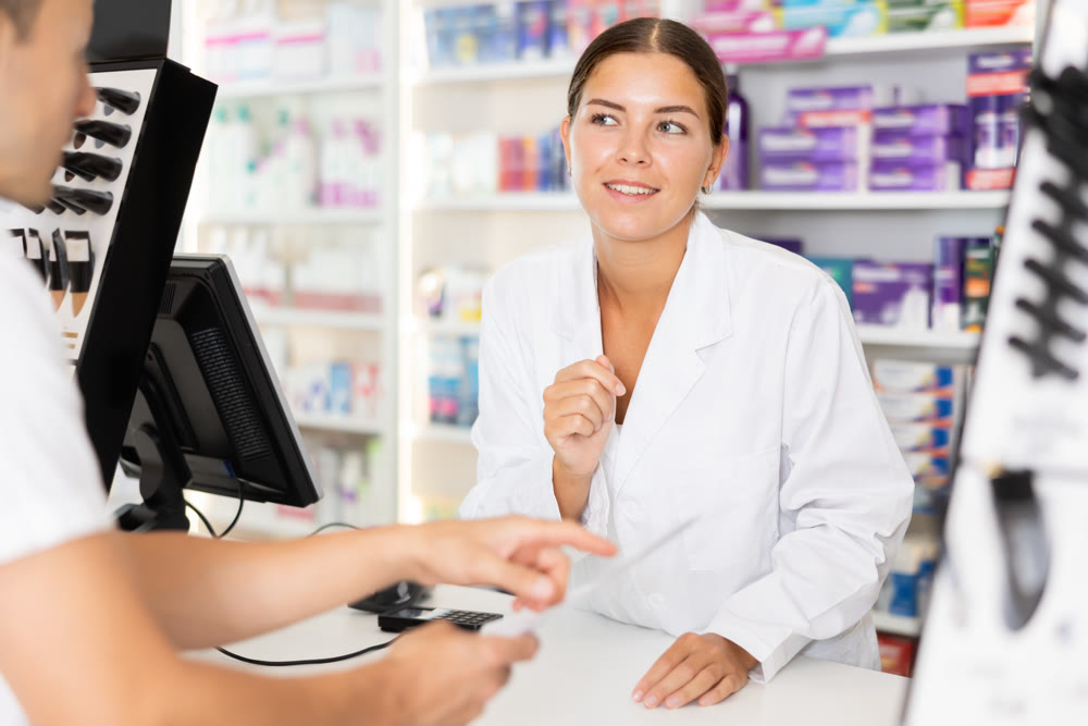 Young female pharmacist serving client buying medicament in drugstore