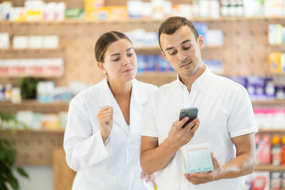Young man customer scanning QR of medicine while female pharmacist consulting him