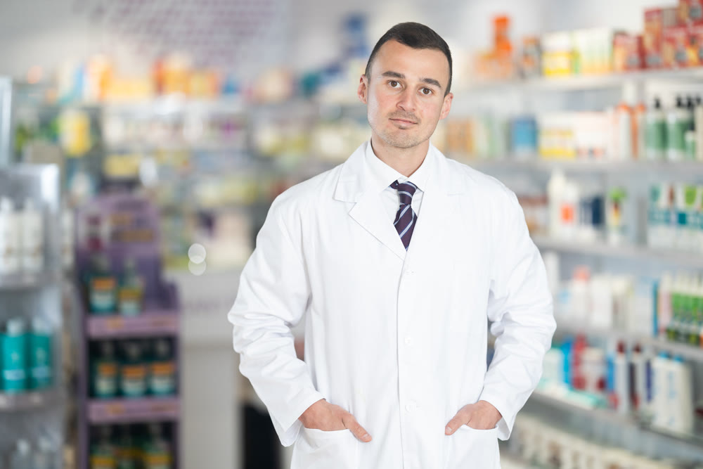 Positive male pharmacist in medical uniform posing while working in pharmacy