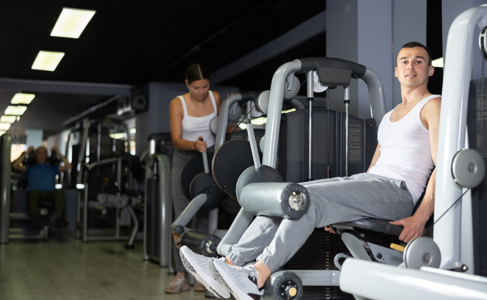 Man in sportswear trains his leg muscles on machine in the gym