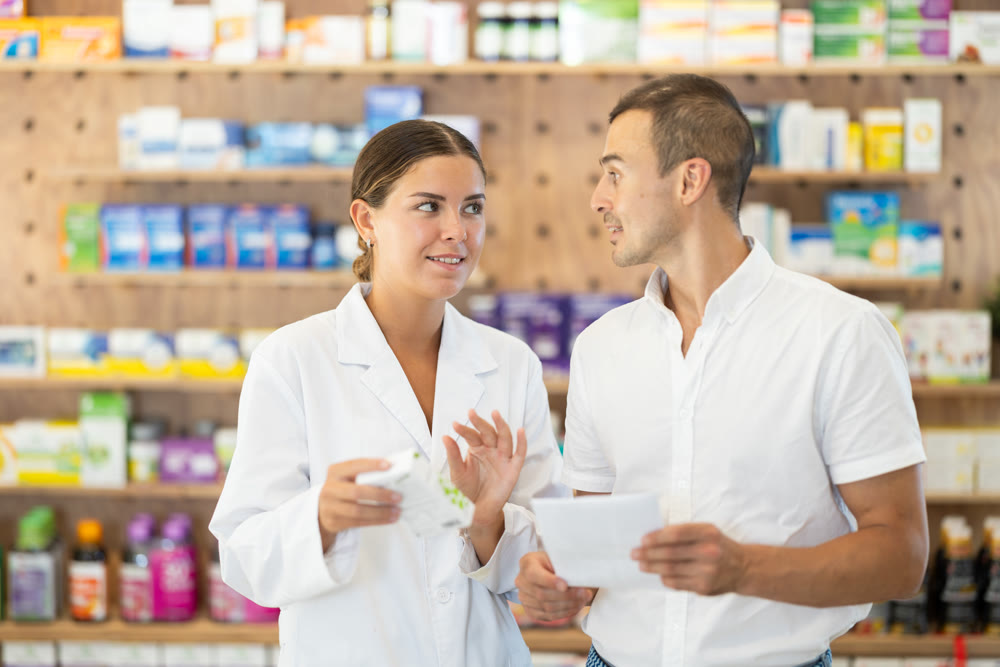 Female pharmacist consulting young guy about medicament according to recipe