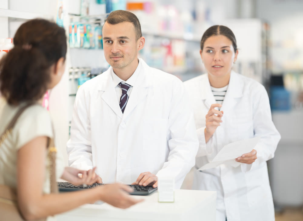 Male and female pharmacists speaking to woman customer buying medical preparation in drugstore