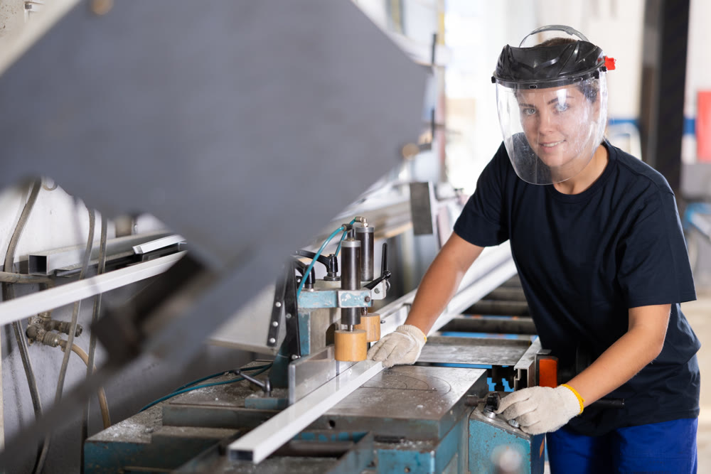 Glass workshop - girl works on machine for cutting aluminum profiles for windows