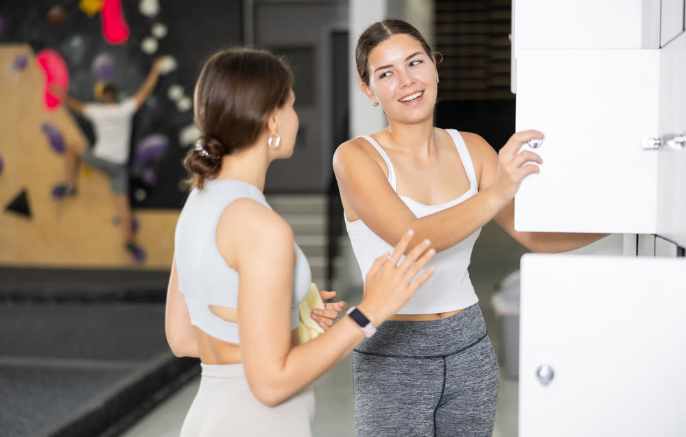 Cheerful girl chatting with female friend by lockers in climbing center