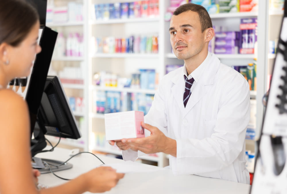 Man pharmacist near cash register area serves customer, scans product and selling drugs