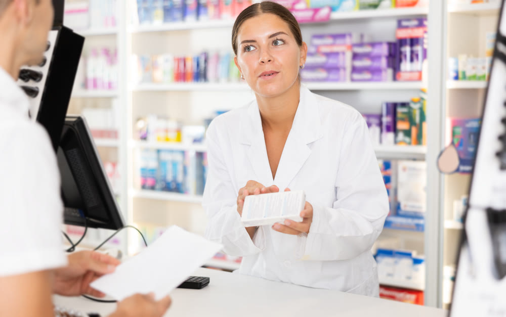 Young female pharmacist serving client buying medicament in drugstore
