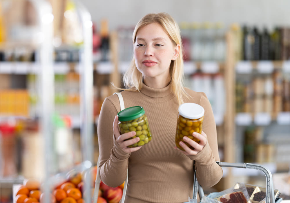 Girl buyer examine good, doubt and choose pickled olives in store