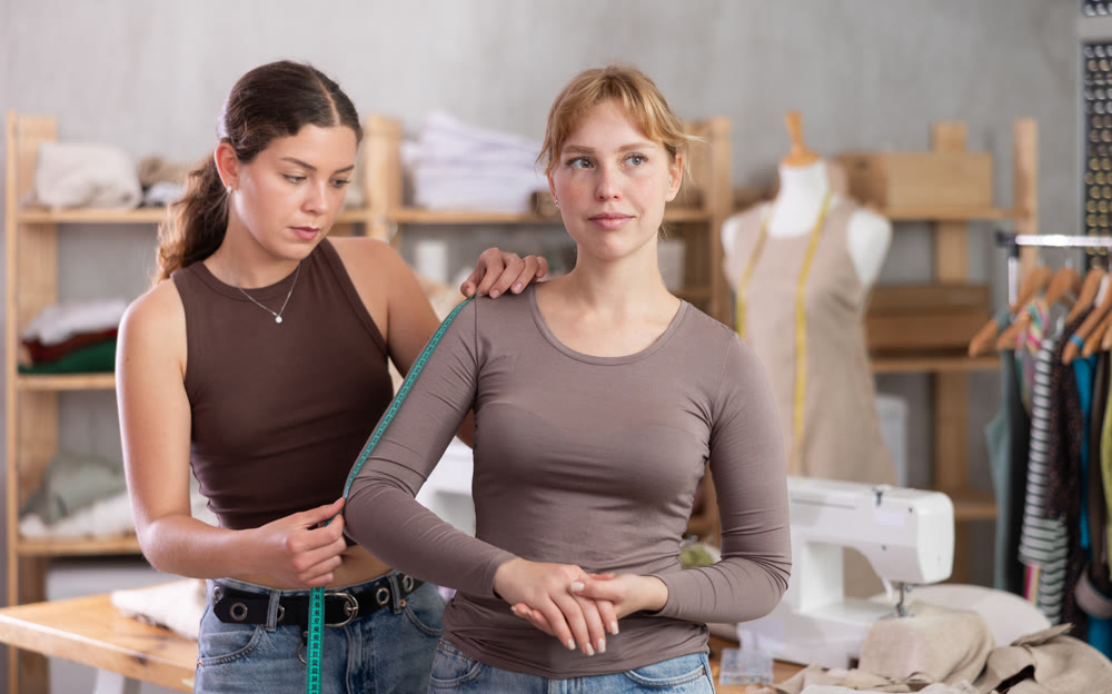 Female dressmaker taking measurements from client in sewing studi