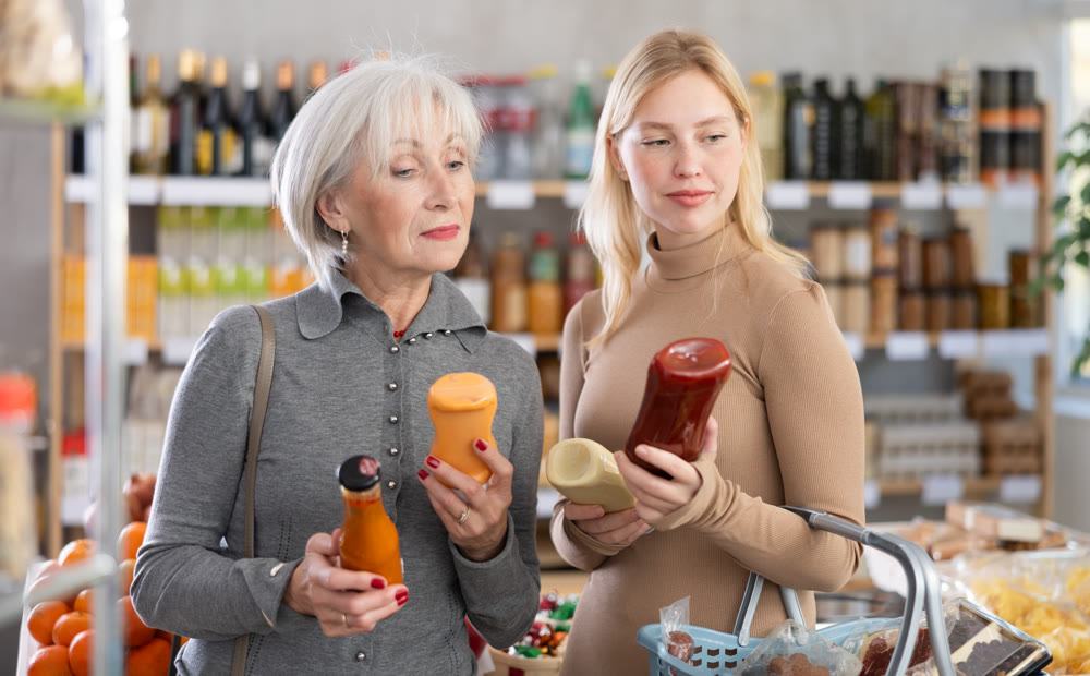 Girl and grandmother buyers examine good, doubt and choose between varieties sauce in store