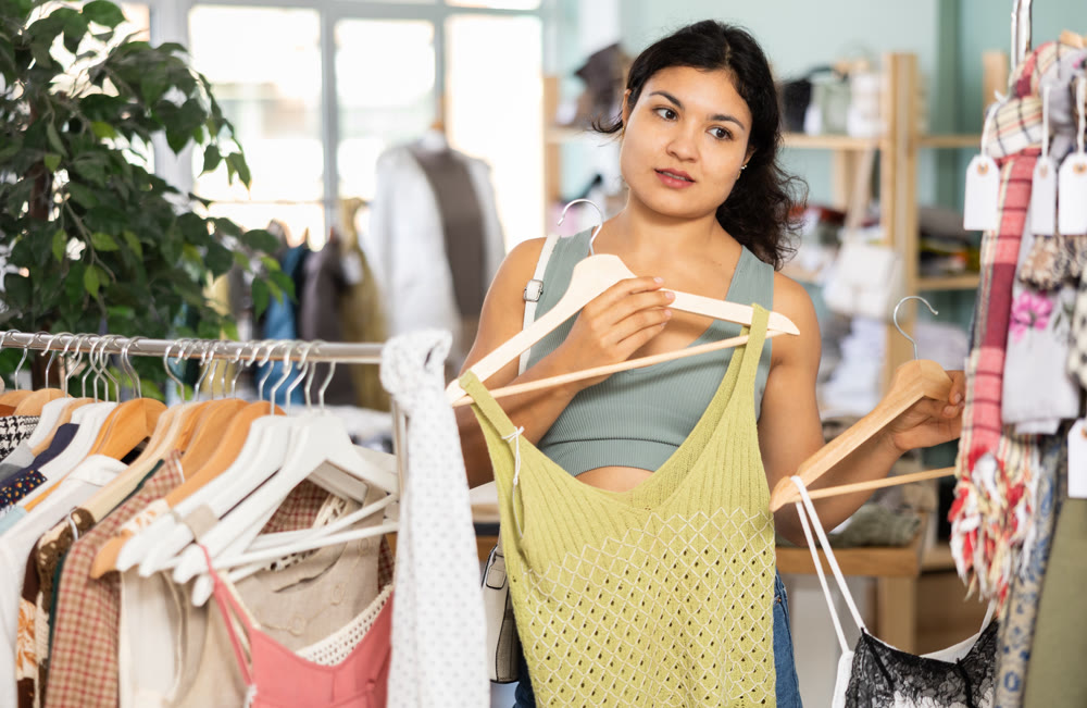Woman chooses dresses or o tops for the summer period in fashionable clothing store