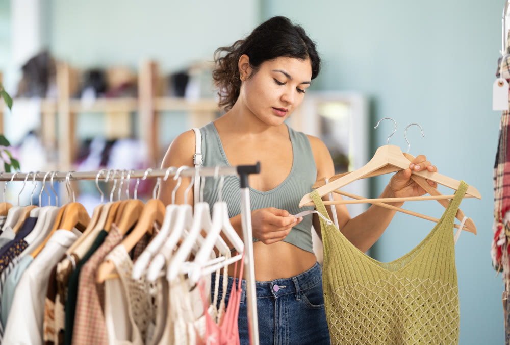 Woman chooses dresses or o tops for the summer period in fashionable clothing store