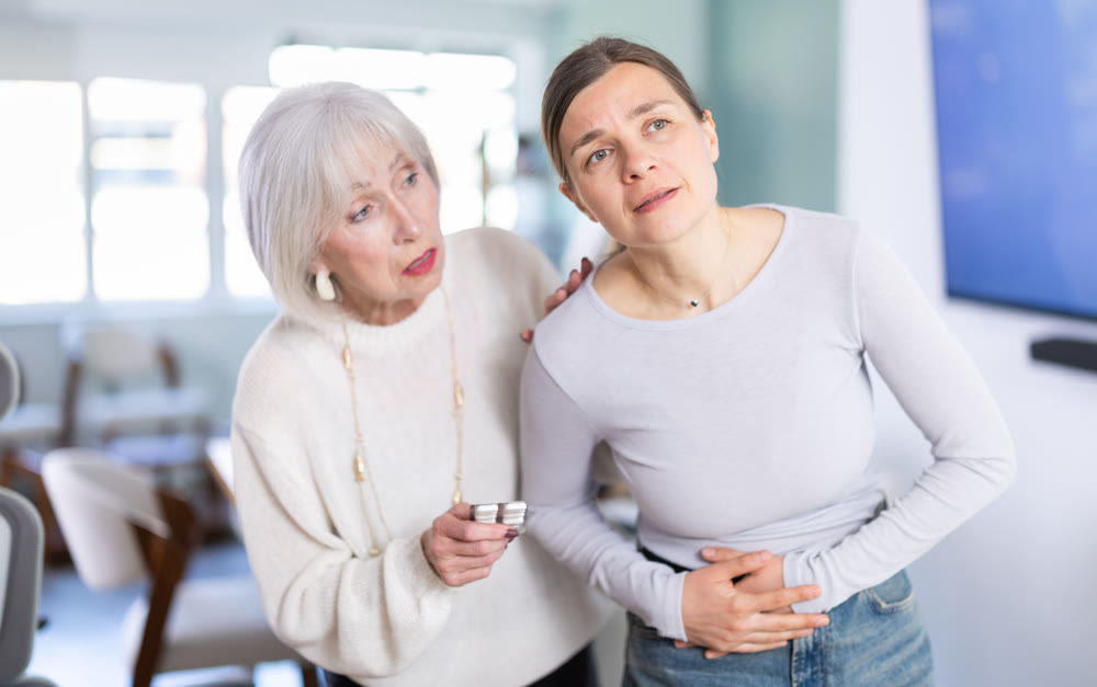 Mature businesswoman offers her colleague abdominal pain pills