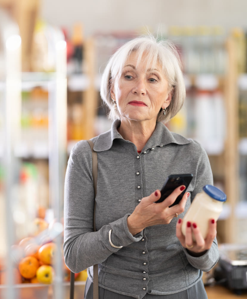 Elderly female shopper scanning QR code on bottle mayonnaise label in grocery department of supermarket