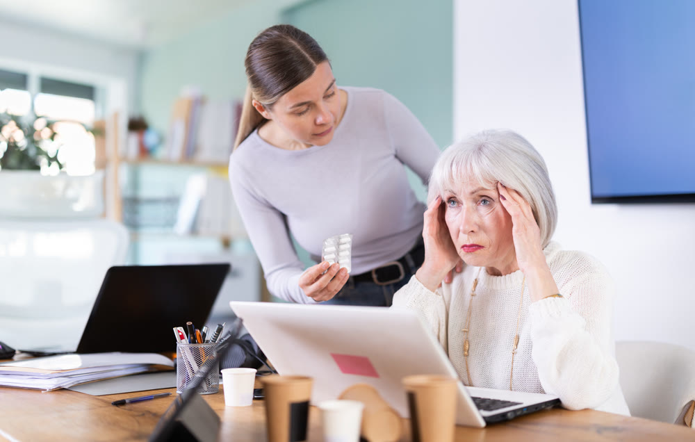 Elderly businesswoman suffers from a headache. Colleague offers her headache pills.