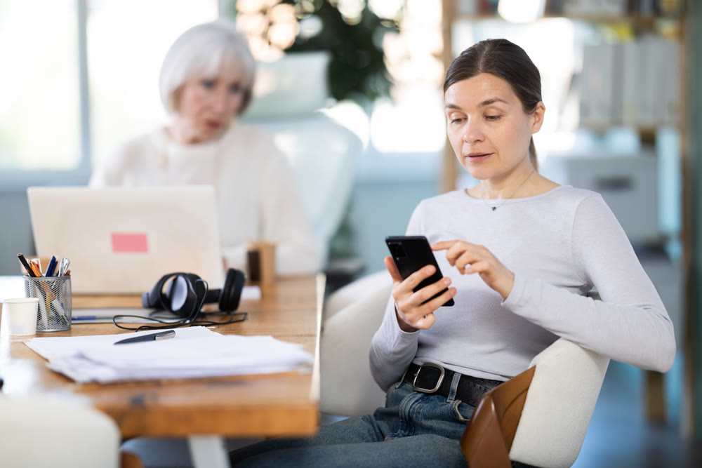 Senior businesswoman complains to subordinate about her talking on her mobile phone while working in office