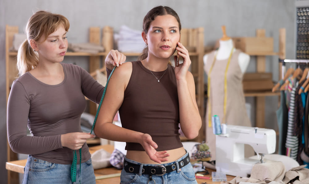 Female customer speaking on phone, while clothing designer taking measurements