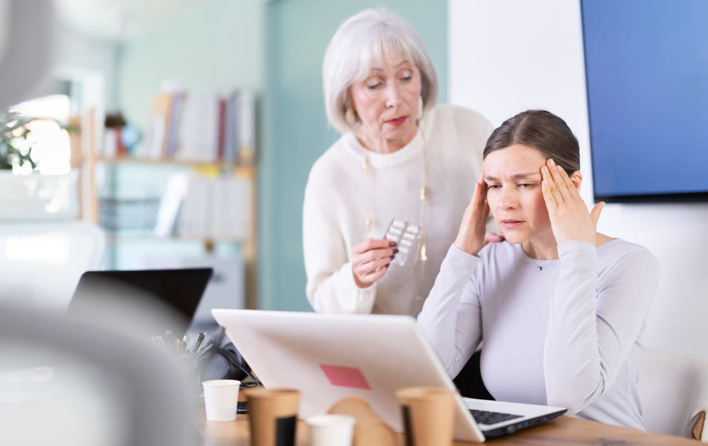 Mature woman sympathizes to sick female manager with headache and offers pain pills.