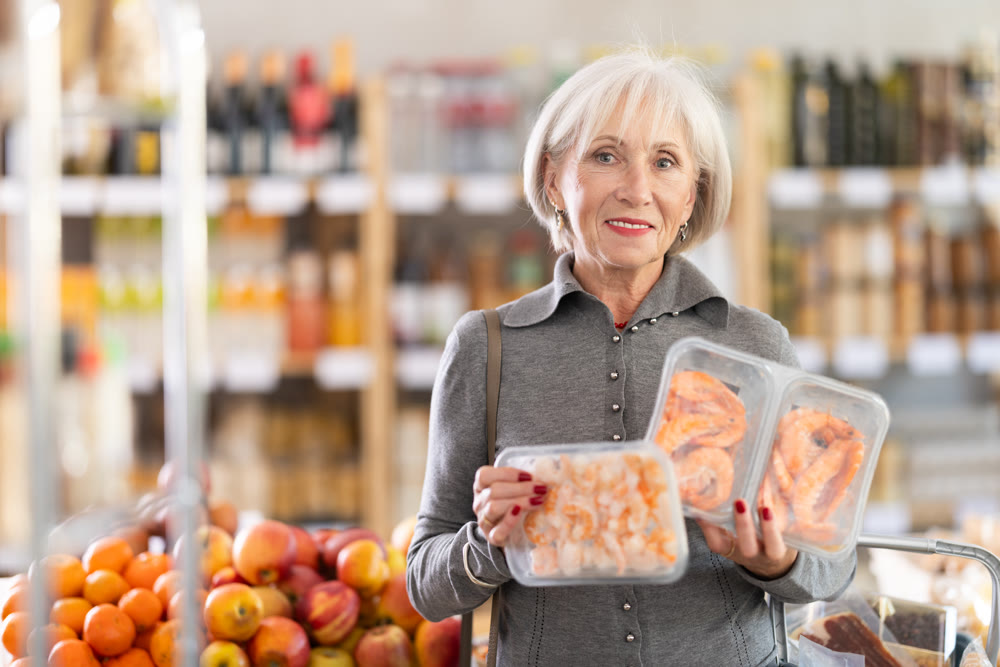 Elderly woman chooses prawns in grocery store