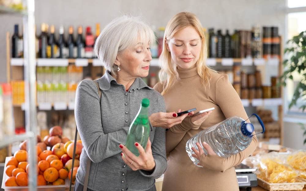Girl and grandmother scan QR code, take reading drinking water label using phone camera in shop
