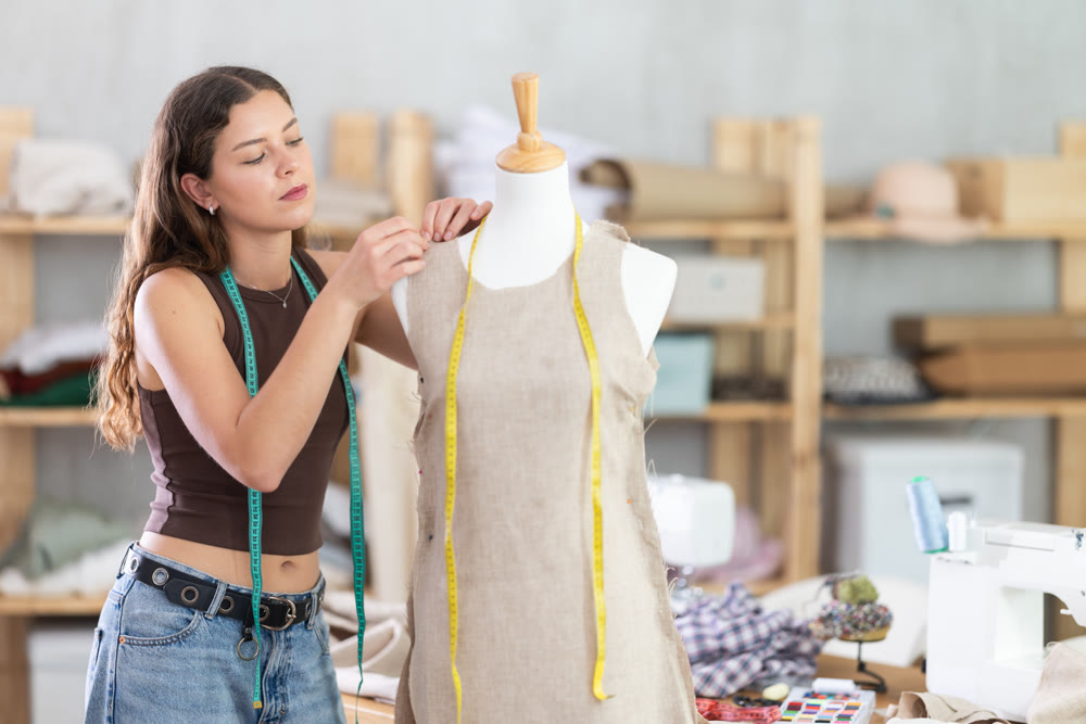 Young female dressmaker working with mannequin in sewing workshop