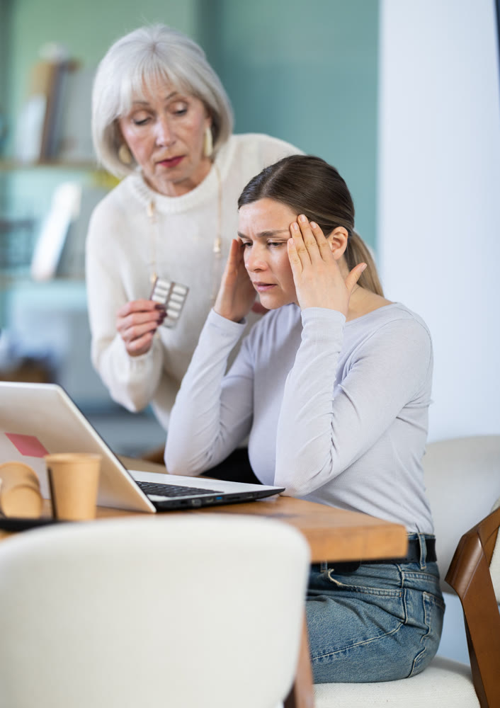 Mature woman sympathizes to sick female manager with headache and offers pain pills.