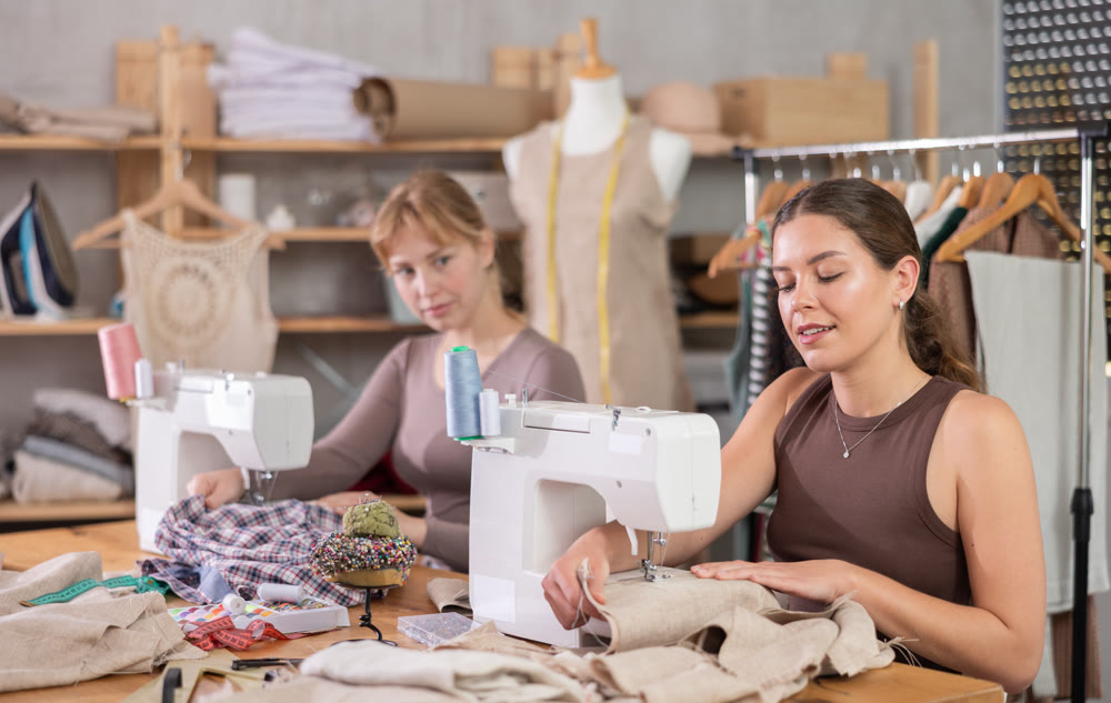 Two female dressmakers working with sewing-machine in tailor's workshop