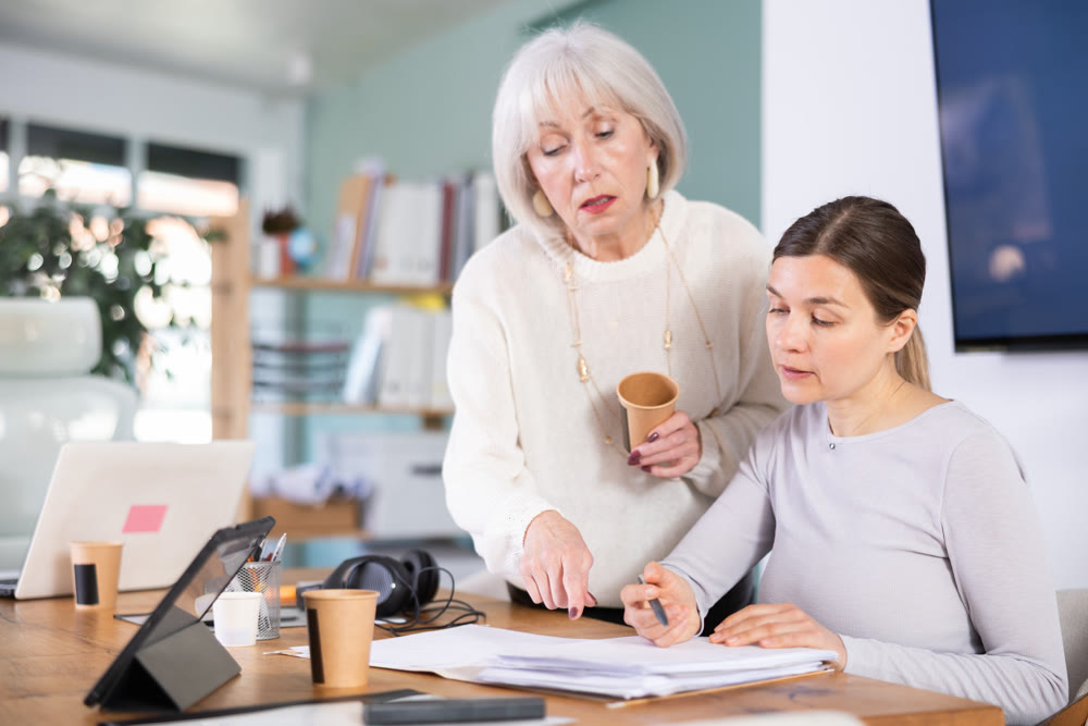 Adult woman taking notes in document elderly colleague helps