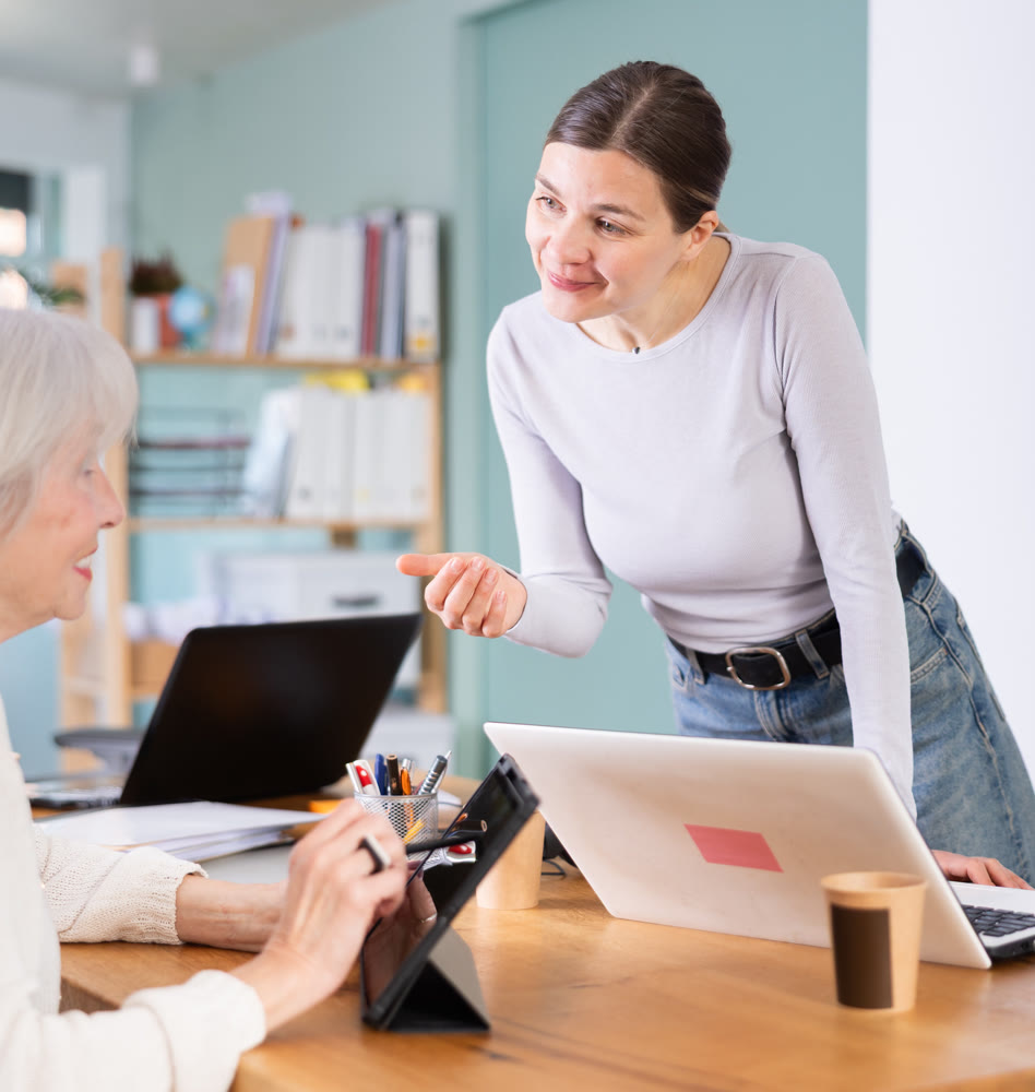 Two businesswomen work on laptops in modern company office