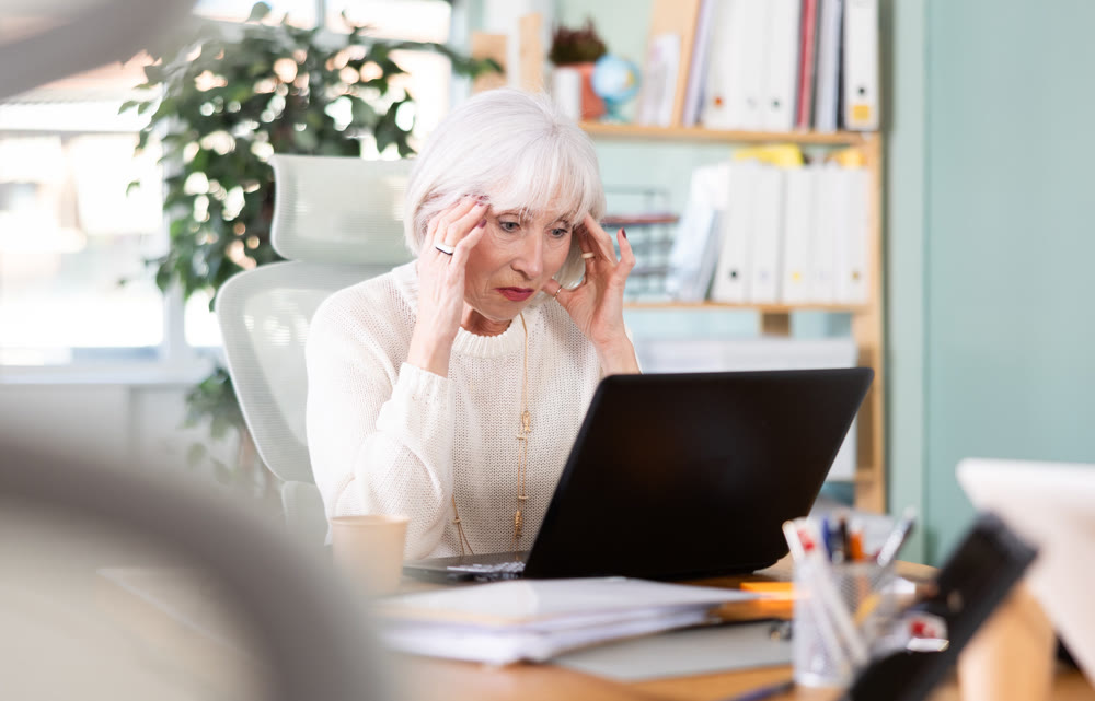 Tired elderly woman works on laptop
