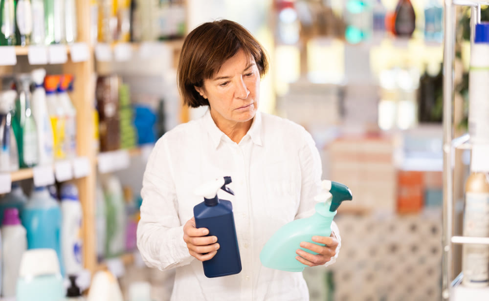 Elderly woman chooses cleaning spray in store