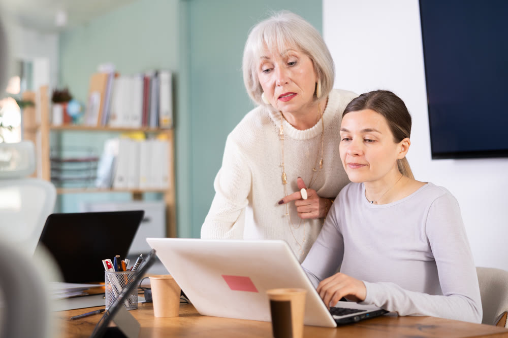 Elderly man help young woman with laptop