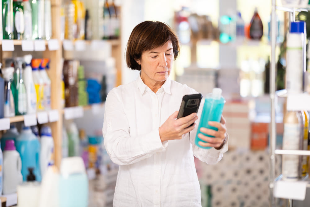 Checking expiration date of shampoo or shower gel - female shopper scans QR code on label of shampoo using smartphone