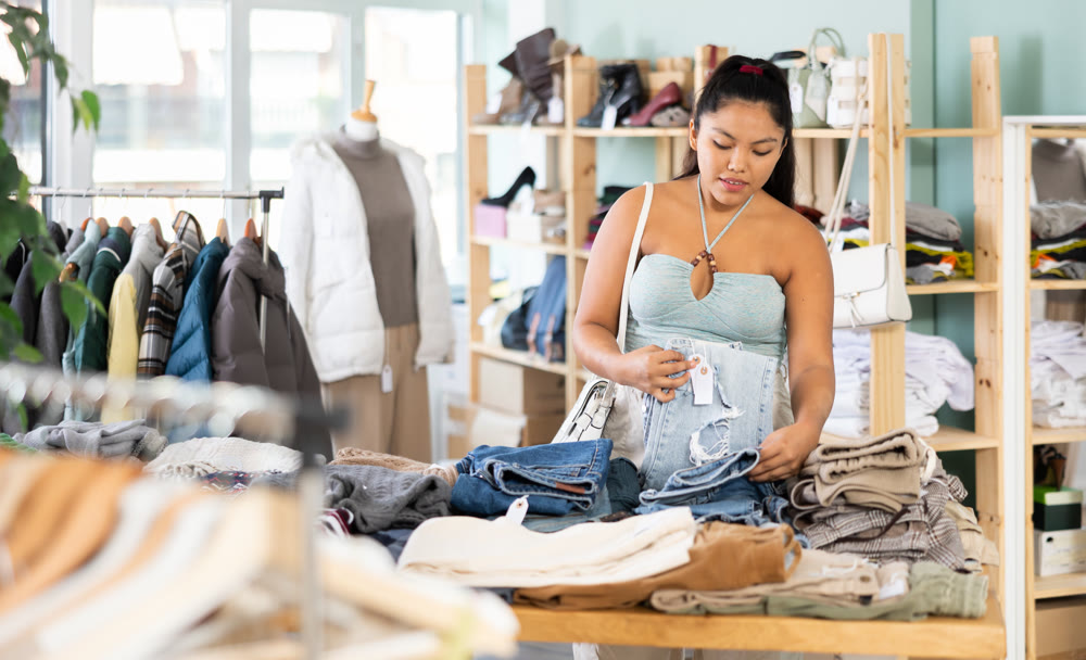 Positive young woman chooses fashionable shorts in clothing store