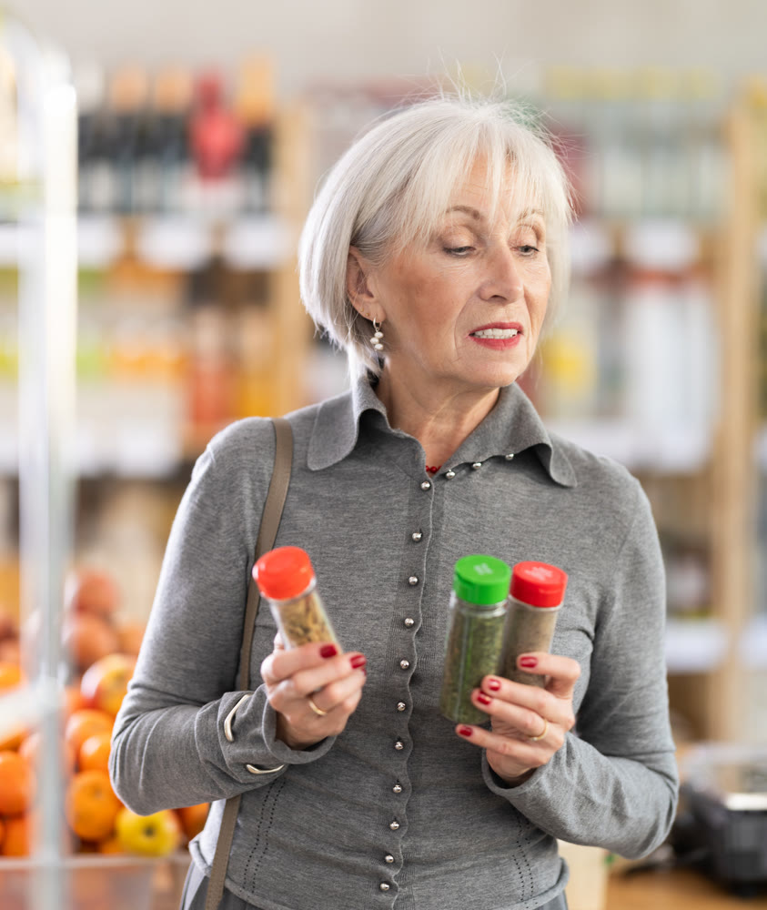 Elderly woman chooses spices and seasonings to buy in grocery department section of store