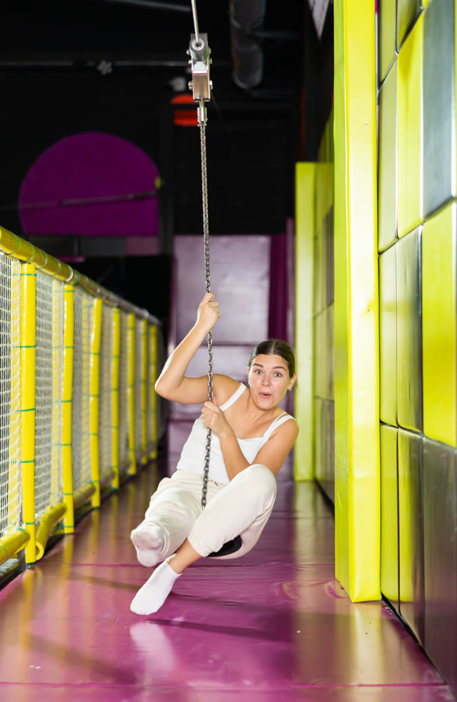 Cheerful young girl riding zip line in indoor amusement center