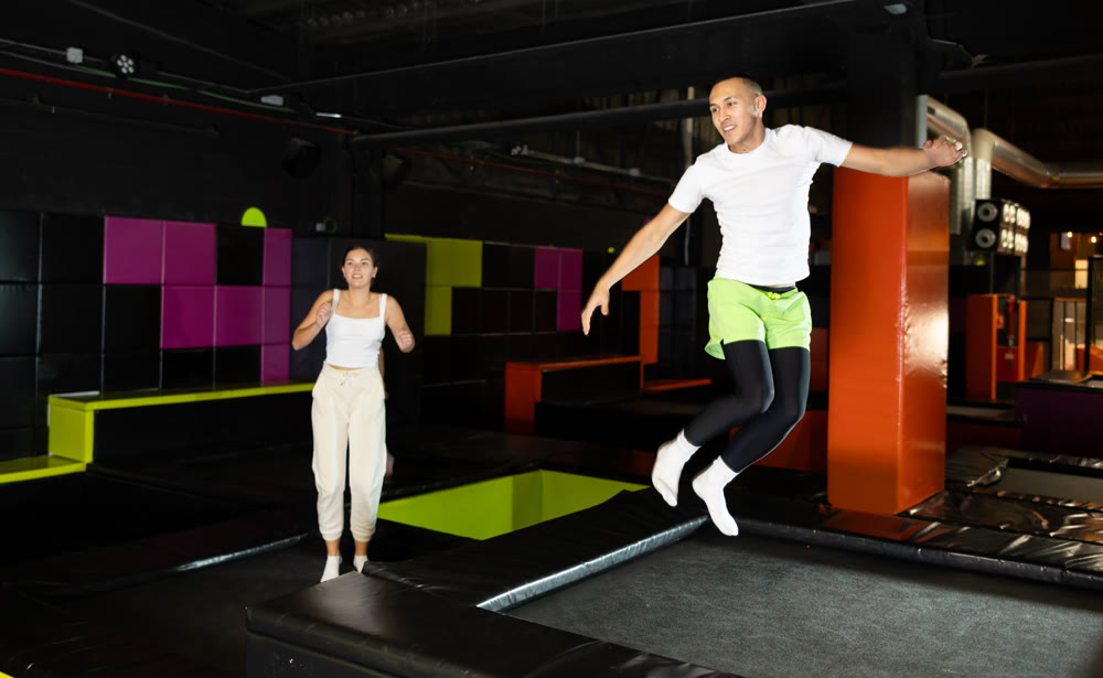 Joyful young man jumping on trampolines in colorful amusement park