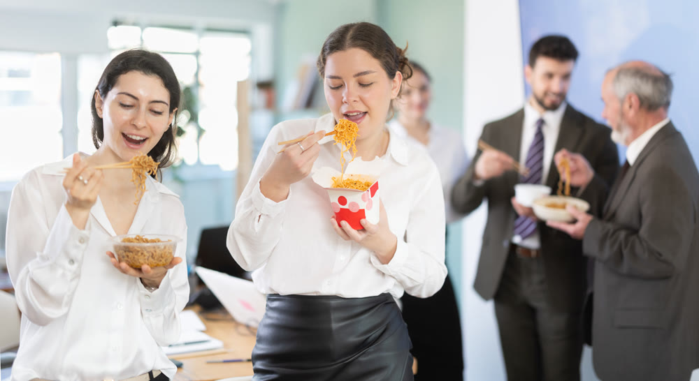 Group of colleagues, man and woman, are having lunch in office during their break, eating noodles