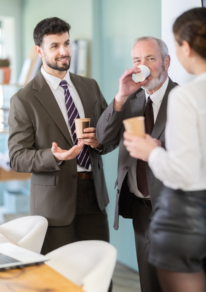 Coffee break - men and young woman drink coffee and chat lively with each other in modern office