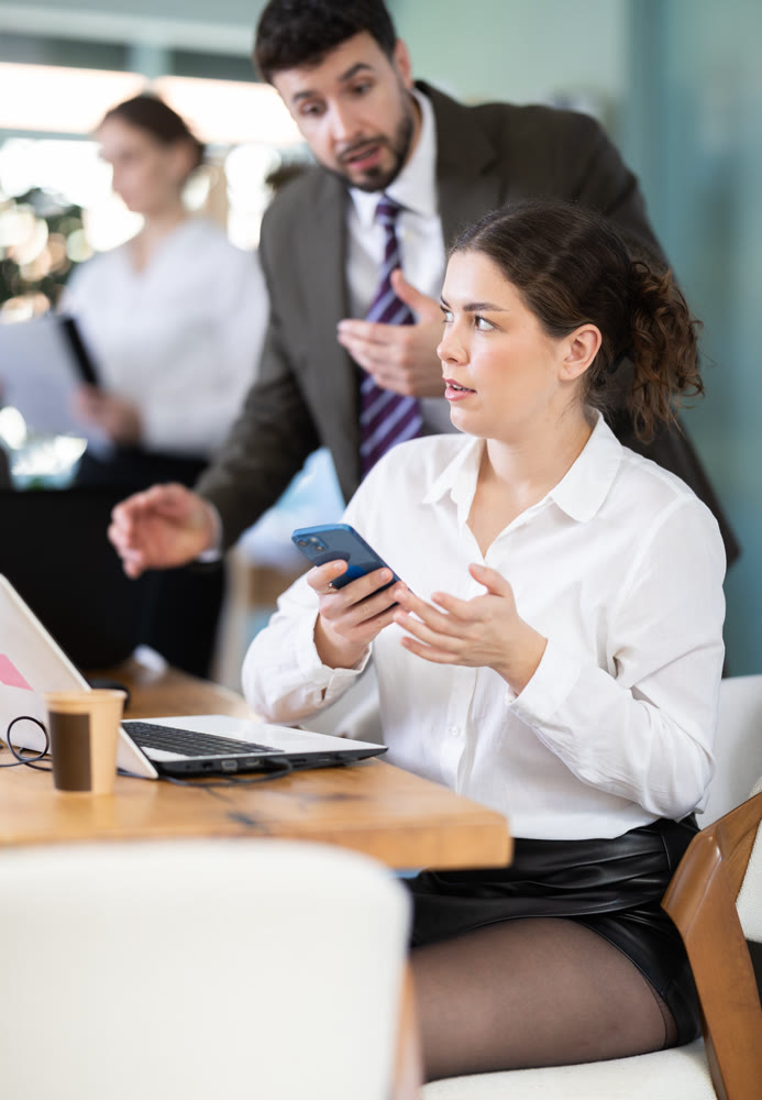 Male boss scolds female employee for scrolling on her smartphone while working in office