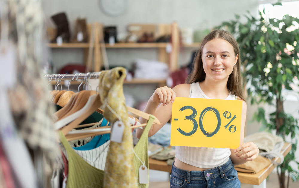 Teen girl holding discount sign in clothing store