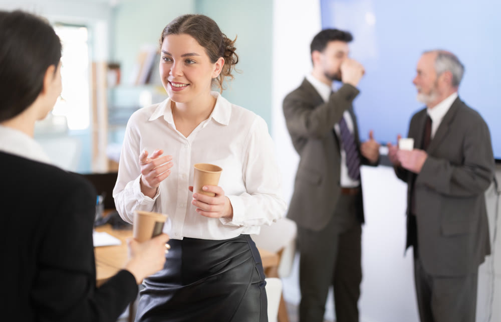 Two girls colleagues chat and laugh during coffee break