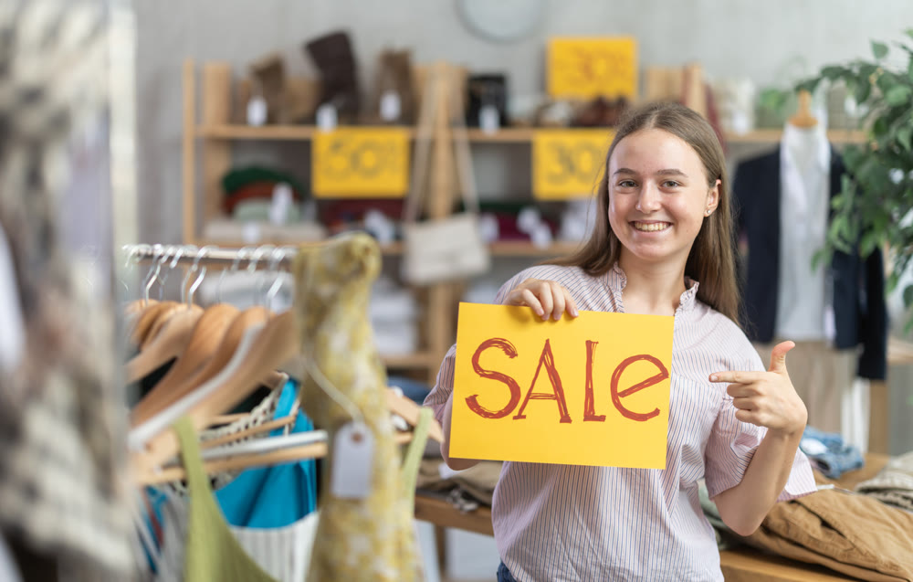 Teenage girl holding sale banner in clothing store