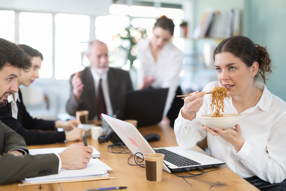 Woman office worker eats noodles while other employees are unhappy with her behavior