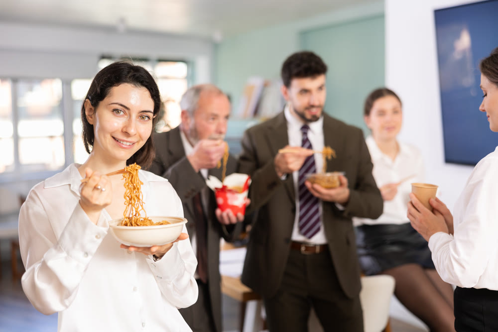 Group of colleagues, man and woman, are having lunch in office during their break, eating noodles