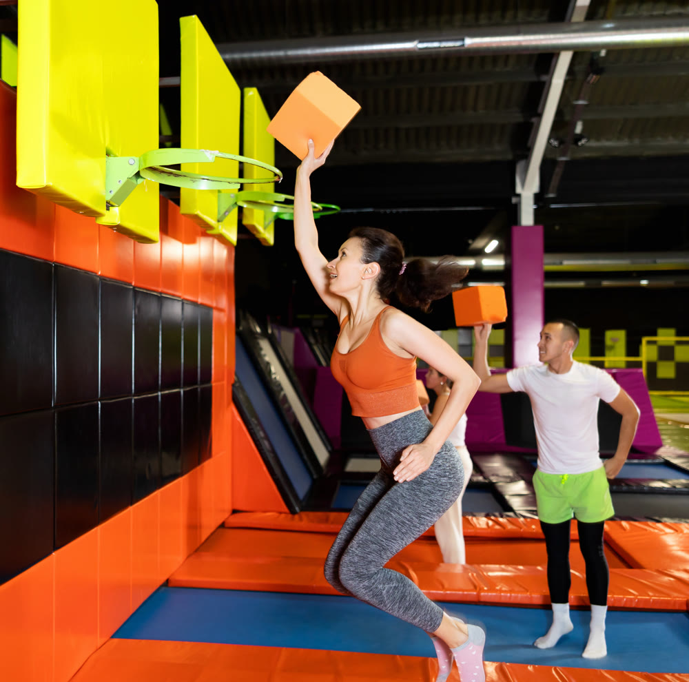 Athletic people throw ball into basketball basket while jumping on trampolines at an entertainment center