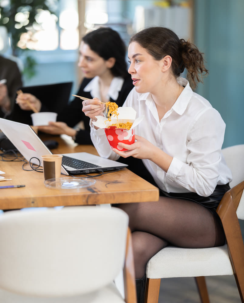 Lunch break - woman eating noodles with colleagues in modern office