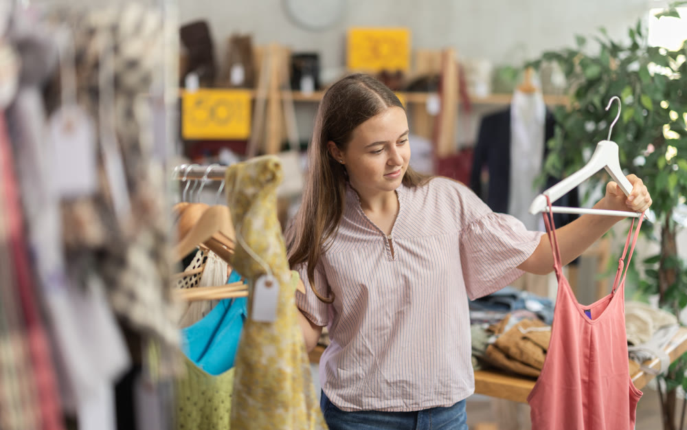 Positive teenage girl choosing something for summer in clothing store