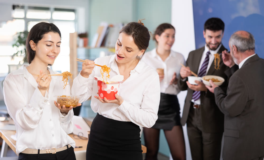 Office workers are eating noodles during their break and chatting with each other
