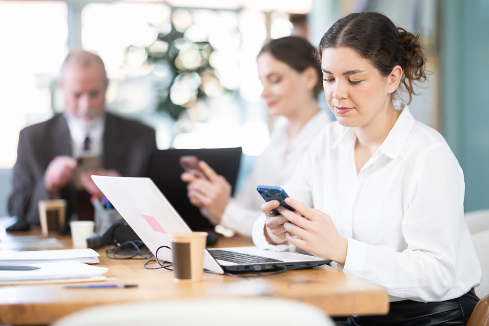 Girl scrolls feed and passes time on social media. Bored staff on smartphone in background